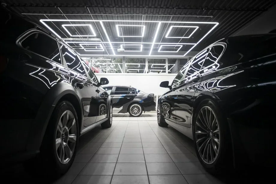 Black cars framed by geometric inspection lights in a detailing showroom